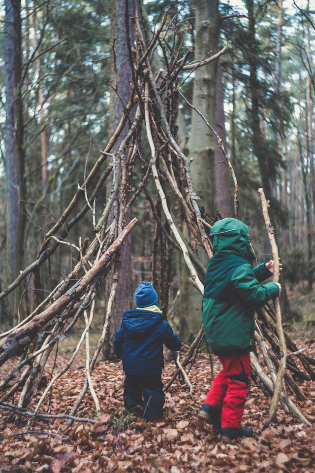 Bilde av to barn i skogen som støtter store pinner mot hverandre.